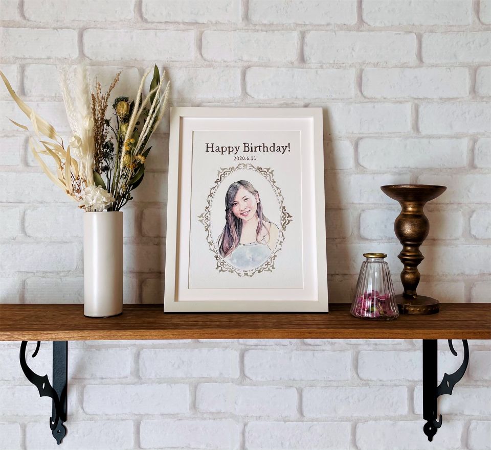 お誕生日祝いの似顔絵展示例。背景は何も描かず、飾り枠の中に女性の笑顔が描かれた似顔絵作品。